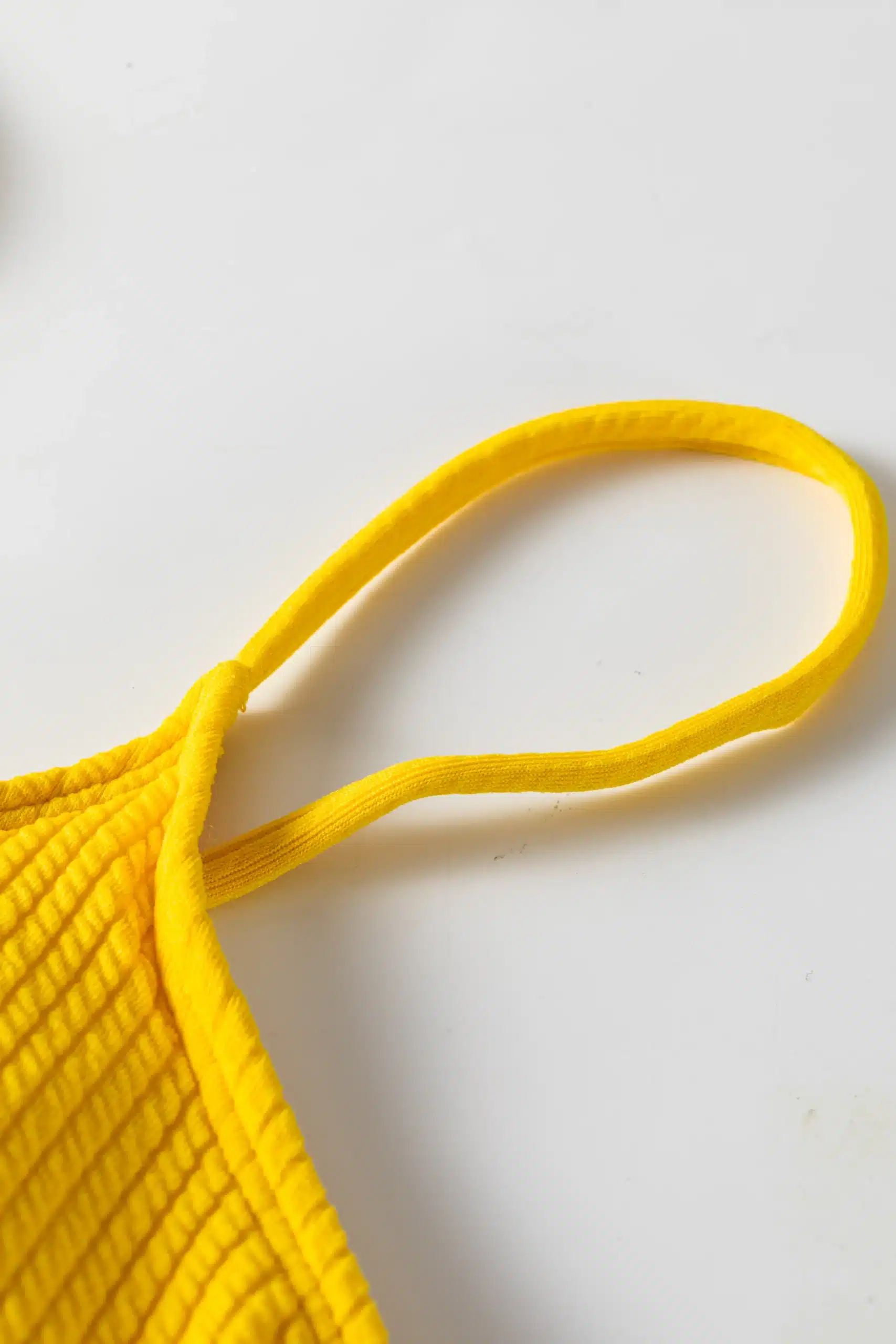 Close-up of the thin elastic yellow shoulder strap sewn into the ribbed fabric of the bikini top.