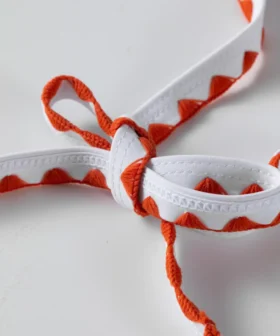 Macro close-up of white bikini tie strings with orange zigzag stitching tied into a neat bow.