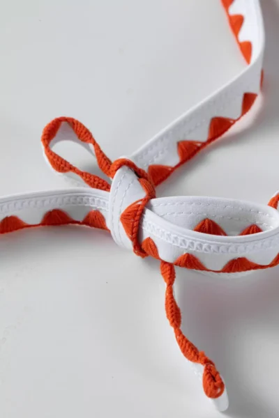 Macro close-up of white bikini tie strings with orange zigzag stitching tied into a neat bow.